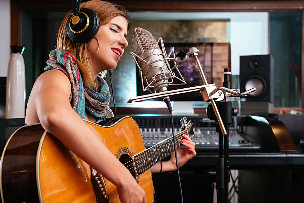 Young woman with guitar recording a song in the studio