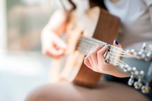 woman hands playing acoustic guitar, close up view