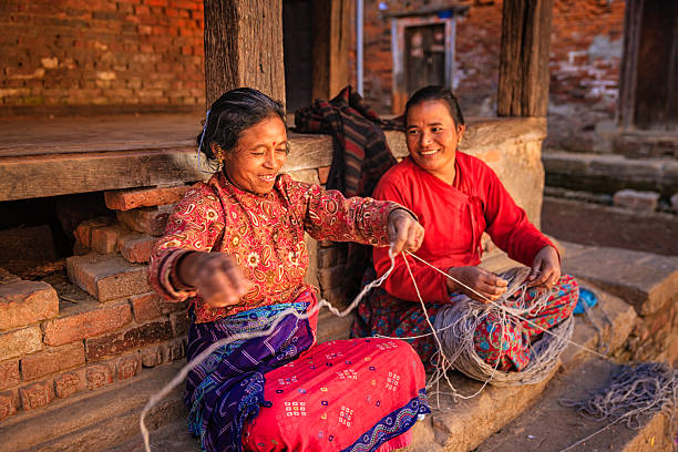 Nepali women spinning a wool in front of the house.